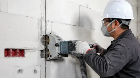 Electrician using wall chaser with dual diamond blades to cut conduit channels in masonry