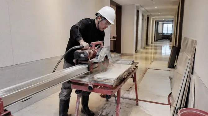 Stone installer doing on-site cutting with a wet-cut rail saw in an occupied commercial building