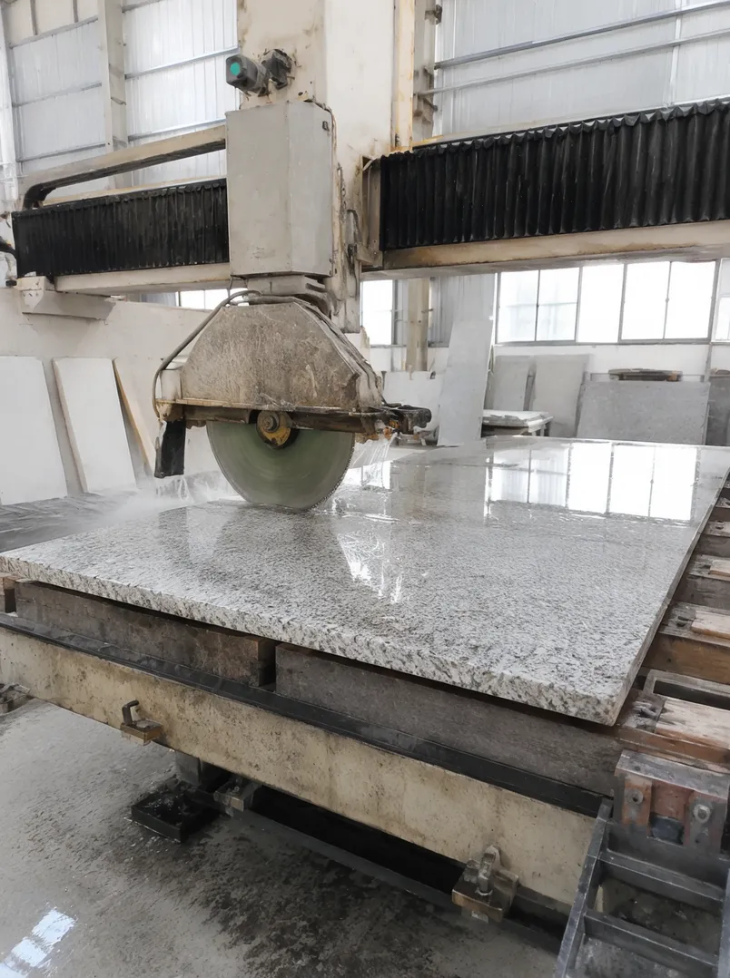 Stone fabrication shop with bridge saw running wet cut diamond blade on granite countertop slab